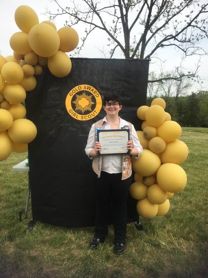 Sammi Ciommo receives Girl Scout Gold Award in Outdoor Ceremony black background gold balloons holding certificate