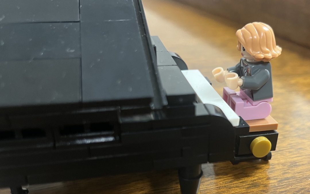 LEGO female minifigure with red bobbed hair playing a logo grand piano